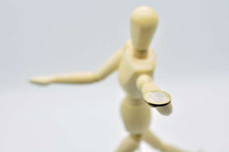 A wooden mannequin holds a coin in his hand. Isolated on white background.の写真素材