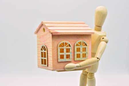 Wooden mannequin carrying a house in his armsの写真素材