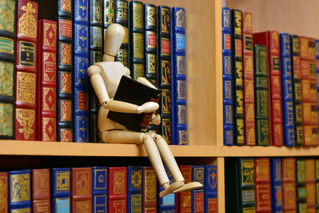 Wooden mannequin reading a book on a library shelf