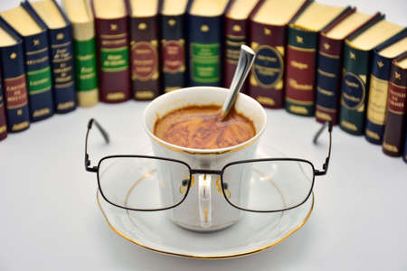 Cup of coffee with glasses, surrounded by booksの写真素材