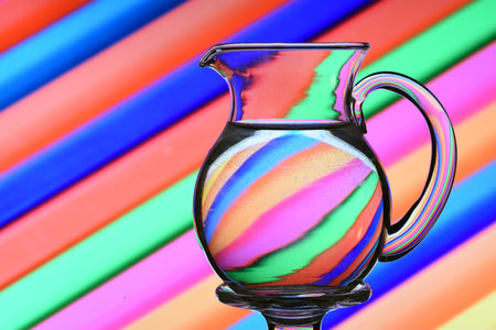 Optical illusion created by refracting light with a pitcher of water and colored diagonal linesの写真素材