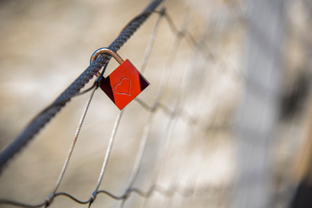 Red padlock, with an engraved heart, hooked on a gate