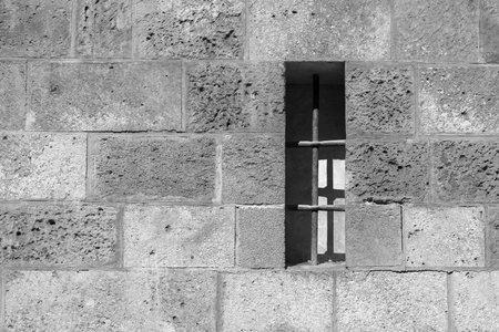 Small window with bars on a wall of a medieval building in black and whiteの写真素材