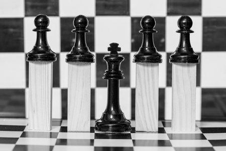 The pawn pieces raised on wooden blocks and the king on a chess board, in black and whiteの写真素材