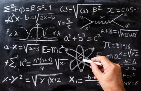Hand writing mathematical operations and quantum physics formulas with a chalk on the blackboard