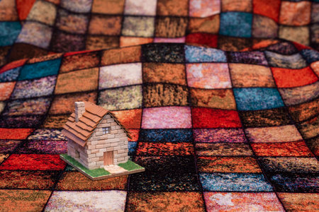 Little house made of miniature stone bricks on a multi-colored checkered fabricの写真素材