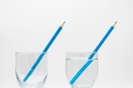 Refraction of light, demonstrated in a glass filled with water and another empty one with colored pencilsの写真素材