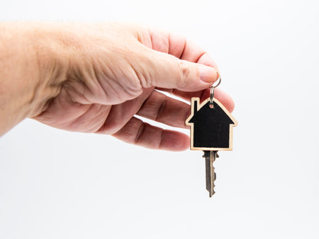 Hand holding a wooden house-shaped keychain with a key, isolated on white