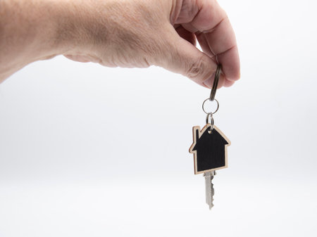 Hand holding a wooden house-shaped keychain with a key, isolated on white