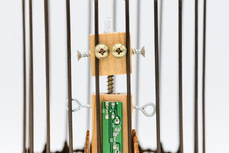 Small robot made of wood and screws inside a cage, isolated on white