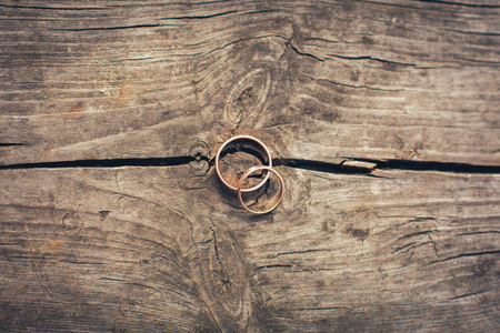 two golden wedding rings lie on a table of dark cracked woodの写真素材