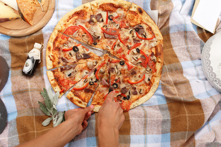 Woman's hands cutting pizza at picnic in sunday parkの写真素材