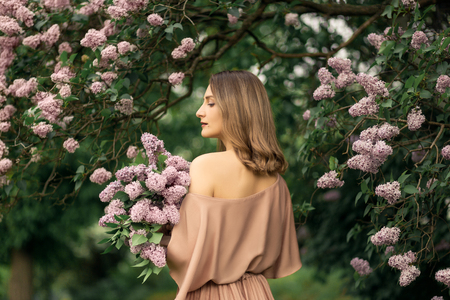 Young woman in a beautiful dress is standing near a lilac bush.の写真素材