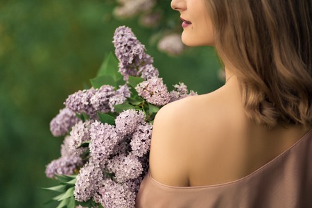 Young woman in a beautiful dress is standing near a lilac bush.の写真素材