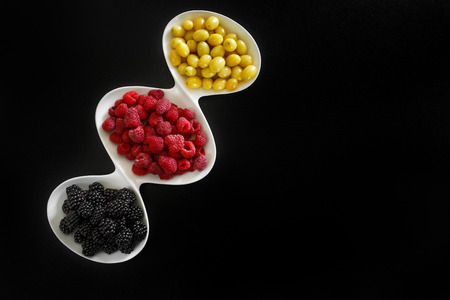 juicy raspberry, blackberries and dogeberry in white plate on black background