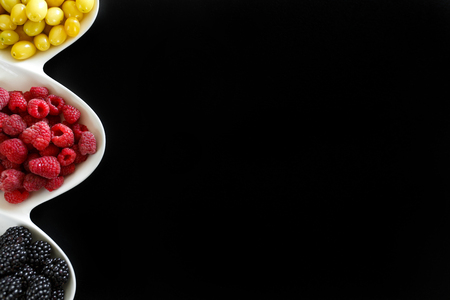 juicy raspberry, blackberries and dogeberry in white plate on black backgroundの写真素材