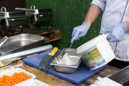 cook in blue gloves on the street puts hummus to prepare falafel in a metal boxの写真素材