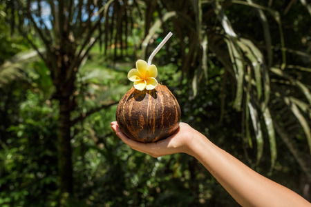 Holding coconut drink in hand at Balinesse jungle background.