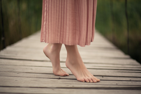 Beautiful tender girl in a peach-colored dress walking on a rural wooden bridge with a bouquet of flowers in hands.の写真素材