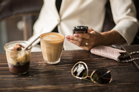 Woman is chatting on the phone while sitting in a cafe with a cup of coffee and dessert.