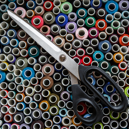 Top view of the box with colored threads on which are large scissors. Sewing industry.