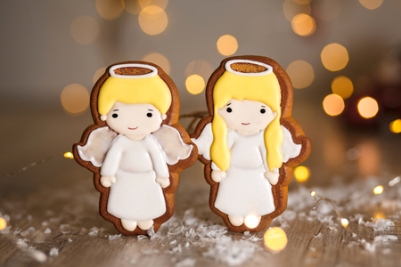 Holiday traditional food bakery. Gingerbread pair of little cute angels boy and girl in cozy warm decoration with garland lights.の写真素材