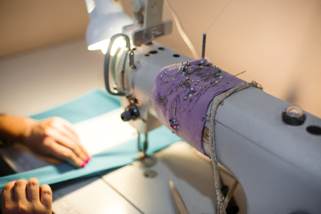 Workplace seamstress. Tailoring industry. Girl sews on the sewing machine. Factory clothing.の写真素材