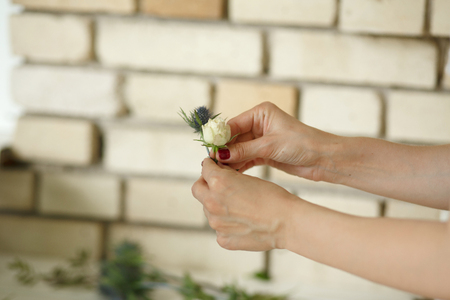Woman florist hands collects flowers for groom boutonniere. Event fresh flowers decoration. Florist workflow. Wedding banquet design.の写真素材