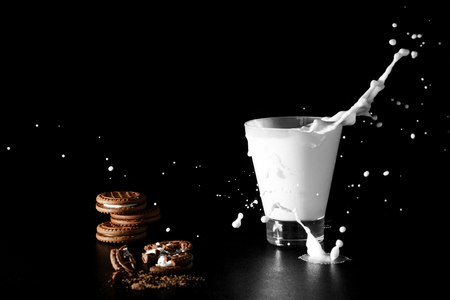 Splash in glass of milk and chocolate cookies on black background.の写真素材