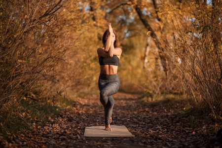 Young woman practicing yoga exercise in autumn park with yellow leaves. Sports and recreation lifestyle.の写真素材