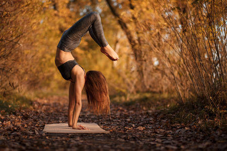 Young woman practicing yoga exercise in autumn park with yellow leaves. Sports and recreation...