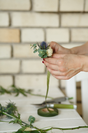 Woman florist hands collects flowers for groom boutonniere. Event fresh flowers decoration. Florist workflow. Wedding banquet design.の写真素材