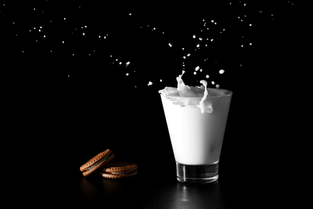 Splash in glass of milk and chocolate cookies on black background.の写真素材