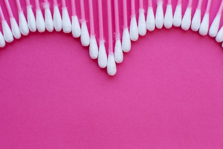 cotton buds laid out in the shape of a heart on a pink background.