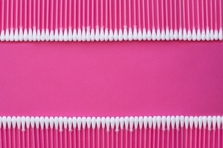 Closeup top view on cotton buds laid in a two horizontal line on pink background.の写真素材
