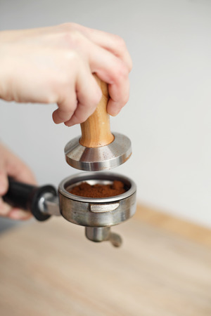 close-up barista hand tamps ground coffee with tamper a into the holder for the coffee machine.の写真素材