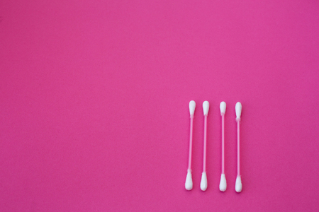 top view on four pink cotton buds with white heads laid out in horizontal line on a pink background.の写真素材