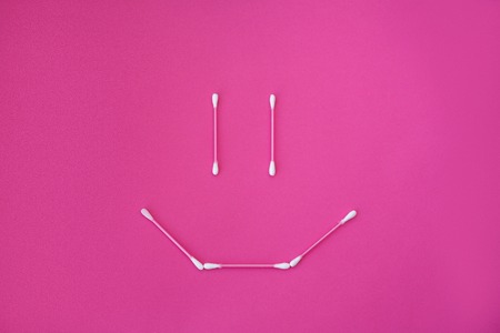 top view on pink cotton buds with white heads laid out in smile face form on a pink background.の写真素材