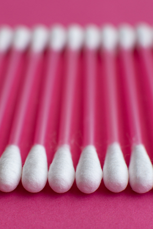 Closeup side view on cotton buds laid in a horizontal line on pink background.の写真素材