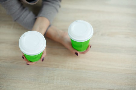 Barista in apron is holding in hands hot coffee in green takeaway paper cup. Coffee take away at...