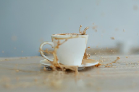 Splash in white cup of coffee on wooden table.の写真素材
