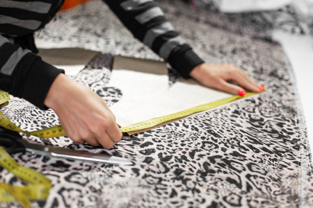 A young girl designer of clothes. Closeup measures by centimeter cut line on the fabric for making...