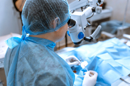 ophthalmologist surgeon looking through surgical microscope doing difficult operation.の写真素材