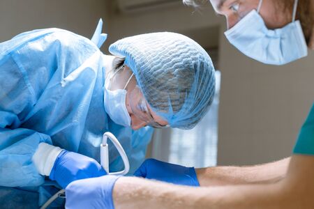 Surgical dentistry. A dentist surgeon treats and removes teeth under anesthesia in the clinic. The assistant helps the surgeon. Sanitation of the oral cavity.の写真素材