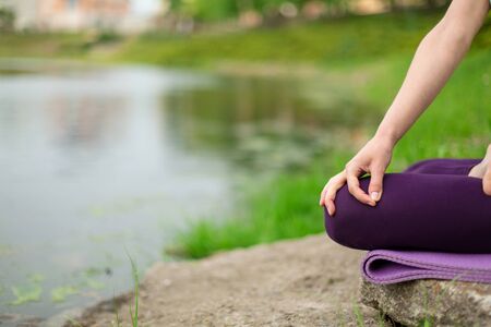 Thin brunette girl plays sports and performs beautiful and sophisticated yoga poses in a summer park. Green lush forest and the river on the background. Woman doing exercises on a yoga mat.の写真素材