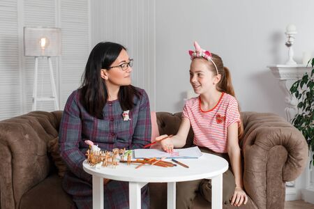 Teen girl on reception at the psychotherapist. Psychotherapy session for children. The psychologist works with the patient. The girl draws pencil with pencil on paper together with a doctor.の写真素材