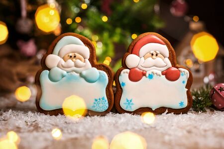 Holiday traditional food bakery. Two gingerbread of santa claus with copy space in cozy warm decoration with garland lights.の写真素材