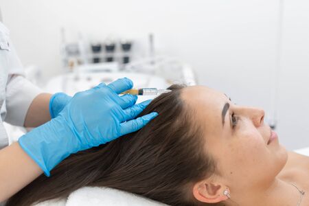 Beautician injections for healthy hair growth. Mesotherapy of the scalp. A young girl is undergoing a course of spa treatments in the office of a beautician. Moisturizing, cleaning and facial skin care. Cosmetic procedures.の写真素材