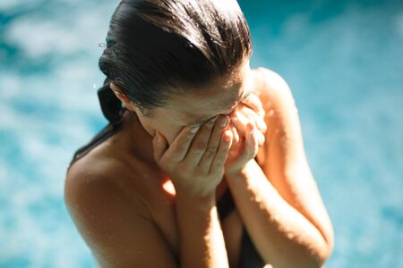 Closeup portrait of sexy slim female wash her face in swimming pool.