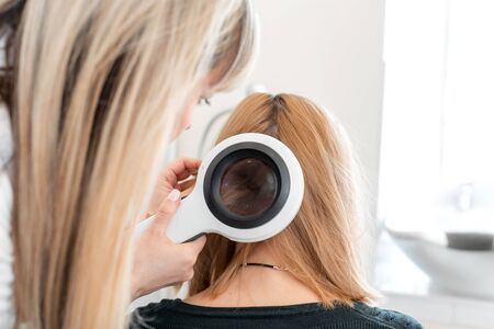 Physician trichologist dermatologist examines the state of the patient's hair and hair roots with a dermatoscope.の写真素材
